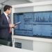 man in corporate attire looking at a wide screen monitor
